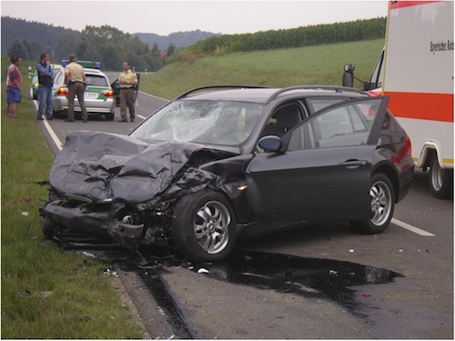 schwarzer PKW Unfallwagen auf einer Landstraße mit Polizei und Rettugnswagen