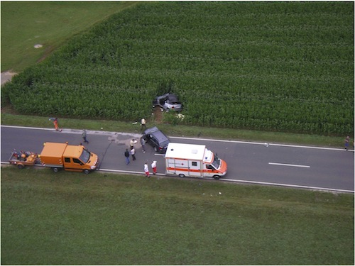 schwarzer PKW Unfallwagen auf einer Landstraße mit Polizei und Rettugnswagen