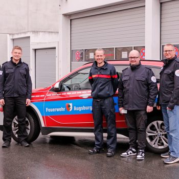 DIe Kollegen der Augsburger Feuerwehr und der TTB der Integrierten Leitstelle Bayreuth Kulmbach beim Besuch in Bayreuth vor einem Dienstfahrzeug der Feuerwehr Augsburg.