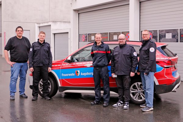 DIe Kollegen der Augsburger Feuerwehr und der TTB der Integrierten Leitstelle Bayreuth Kulmbach beim Besuch in Bayreuth vor einem Dienstfahrzeug der Feuerwehr Augsburg.